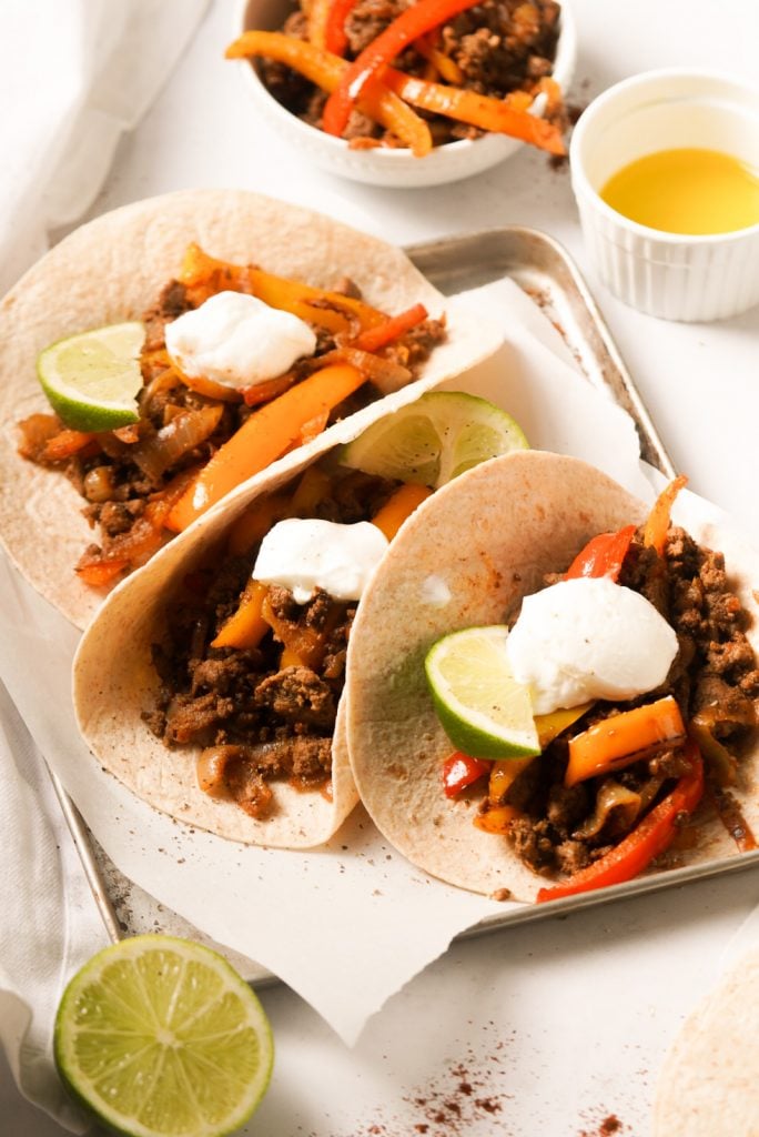 ground beef fajitas on a tray with sour cream and lime