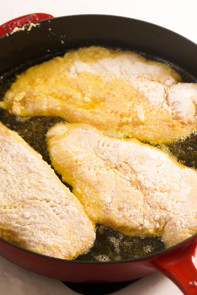 Romano cheese coated chicken breasts pan frying in a large skillet