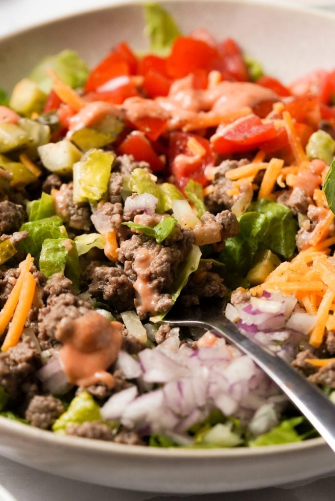 close up shot of salad with seasoned ground beef, cheddar cheese, red onion, tomatoes, pickles