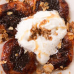 air fryer peaches on a serving plate topped with a big dollop of whipped cream, a drizzle of honey, and cinnamon oat granola.