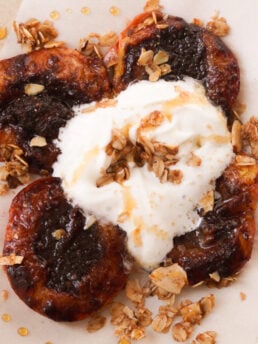 air fryer peaches on a serving plate topped with a big dollop of whipped cream, a drizzle of honey, and cinnamon oat granola.