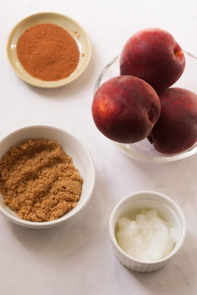 ingredients needed to make air fryer peaches with cinnamon measured out into bowls on a white table.