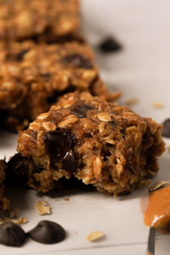Side-on shot of healthy peanut butter chocolate chip oatmeal bar with a bite taken out showing a gooey chocolate chip.
