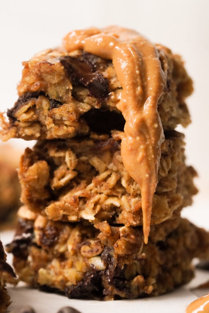 Closeup side-on hero shot of a stack of banana oatmeal breakfast bars studded with chocolate chips and garnished with a dollop of natural peanut butter.