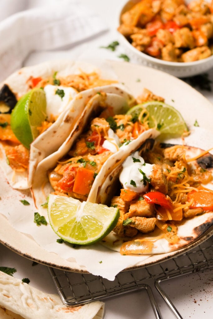 45 degree angle shot of plated chicken fajita tacos with a bowl of chicken and fajita veggies in the background.