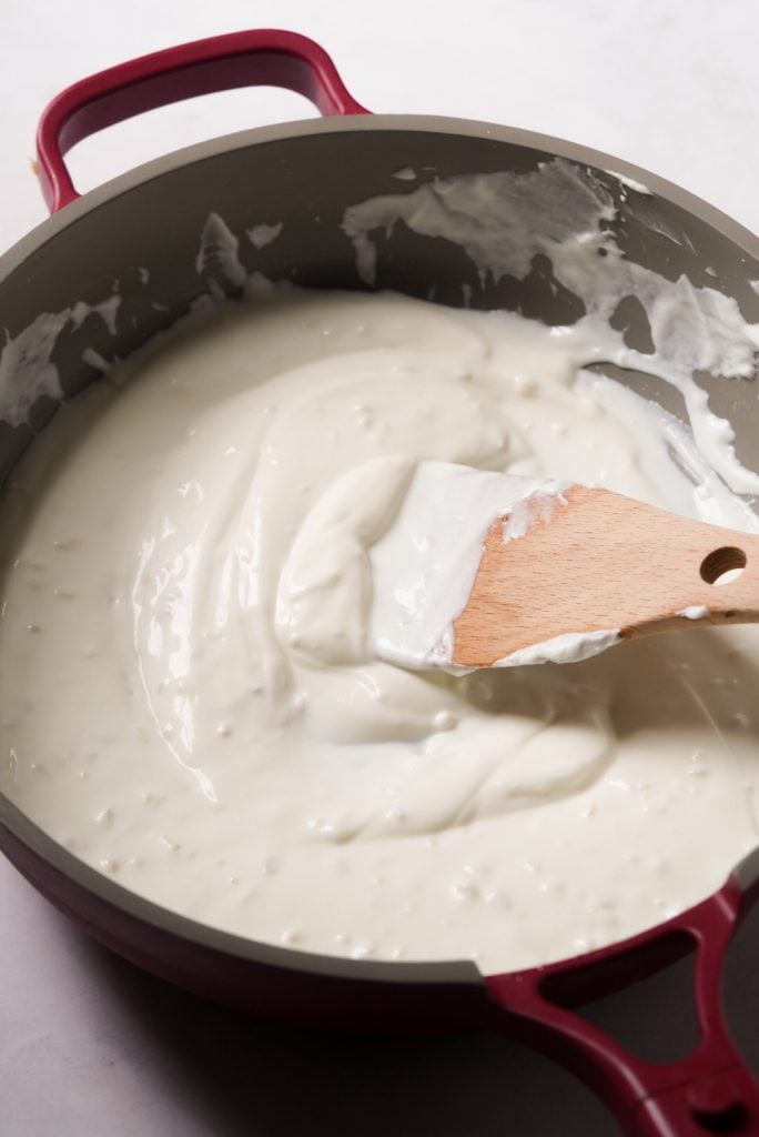 greek yogurt being stirred into healthier alfredo sauce in a pan