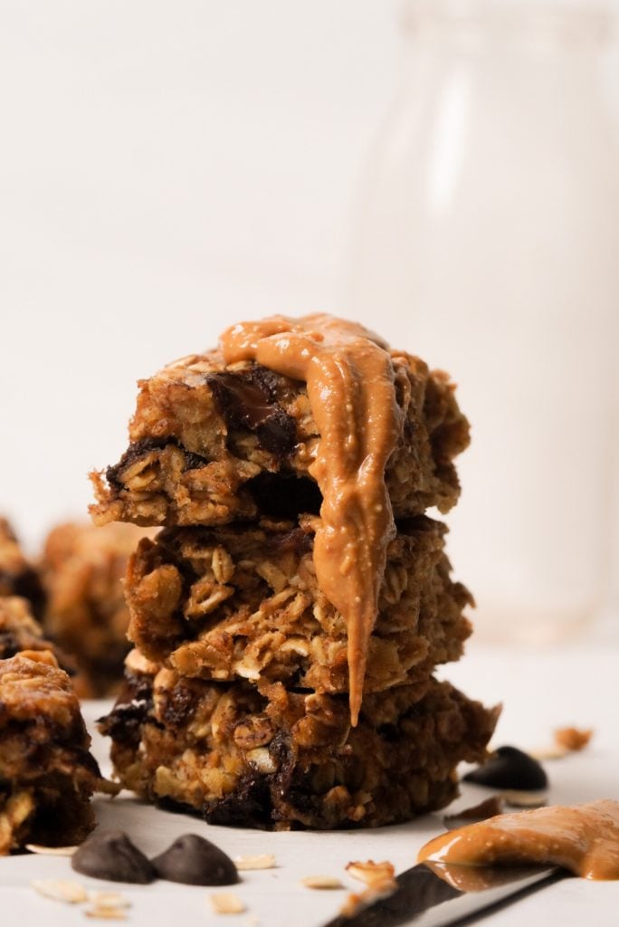 Stack of peanut butter banana oatmeal bars with a dollop of peanut butter running down the side and a glass jug of milk in the background.