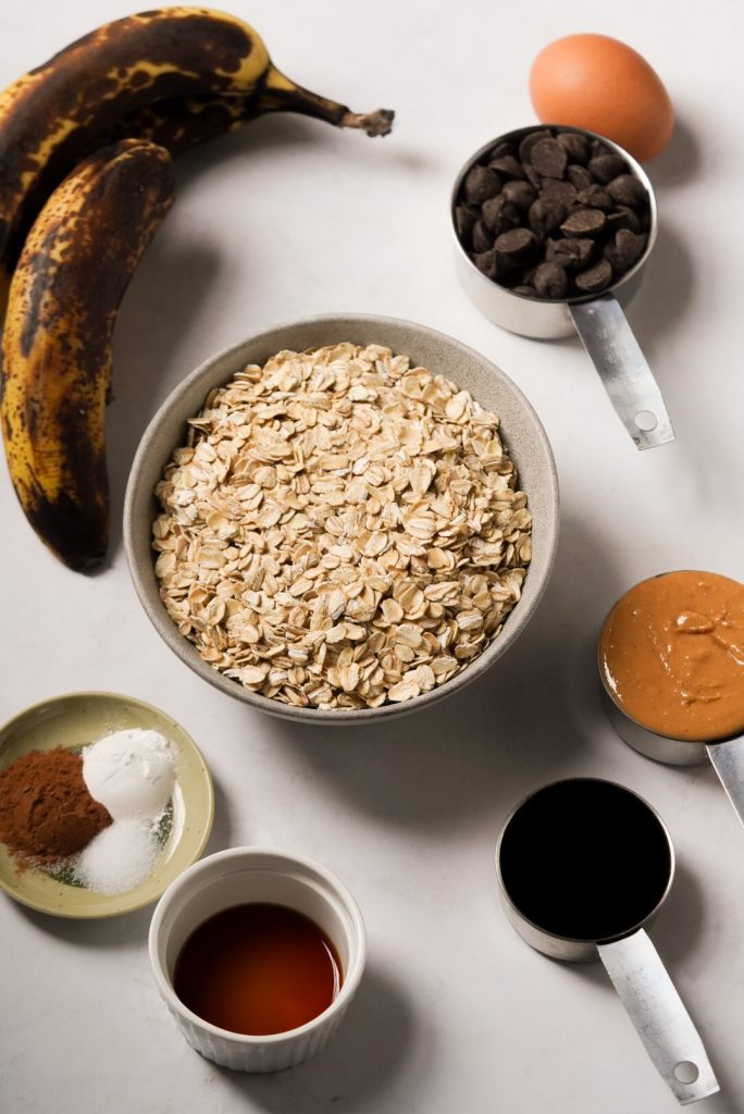 Ingredients needed to make healthy peanut butter banana oatmeal bars measured out into bowls on a white table.