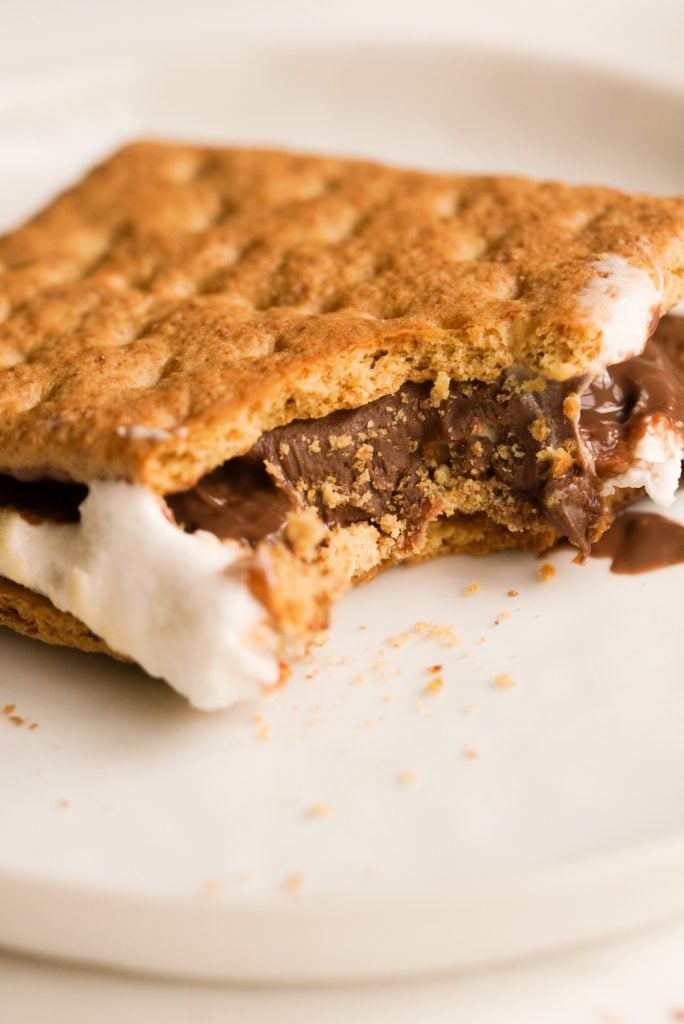 one s'more on a white plate with a bite taken out