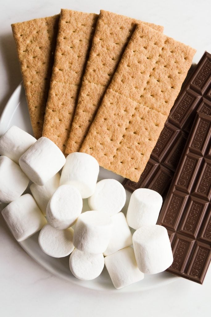 a white plate with graham crackers, Hershey's chocolate bars, and marshmallows on it