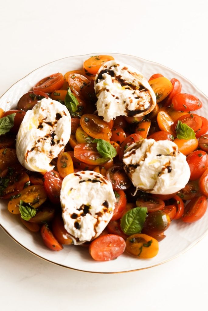 hero image of burrata caprese salad with cherry tomatoes on a white plate.