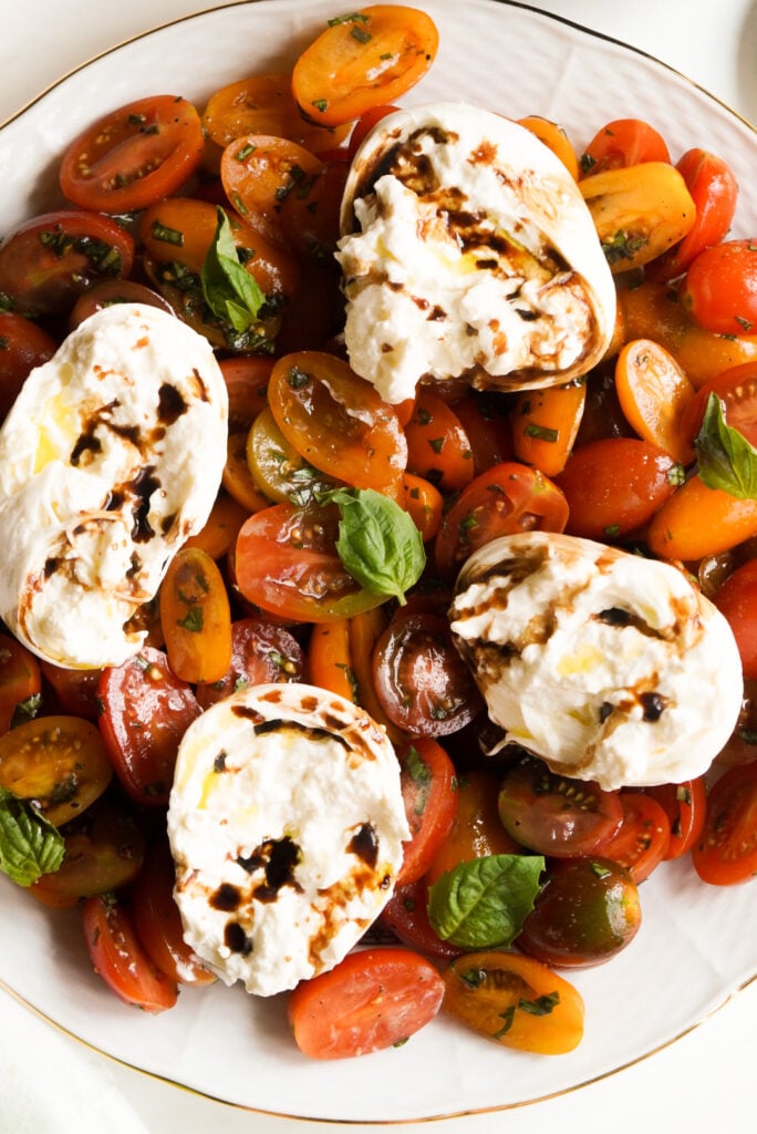 overhead shot of assembled caprese salad topped with halved rounds of burrata and drizzled with balsamic vinegar.