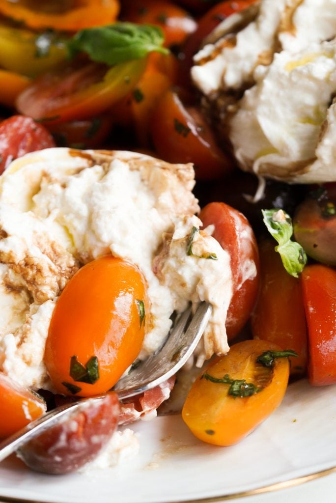 closeup shot of a forkful of burrata cherry tomato caprese salad.