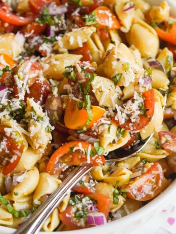super closeup shot of bruschetta pasta salad in a white serving bowl with a silver spoon.