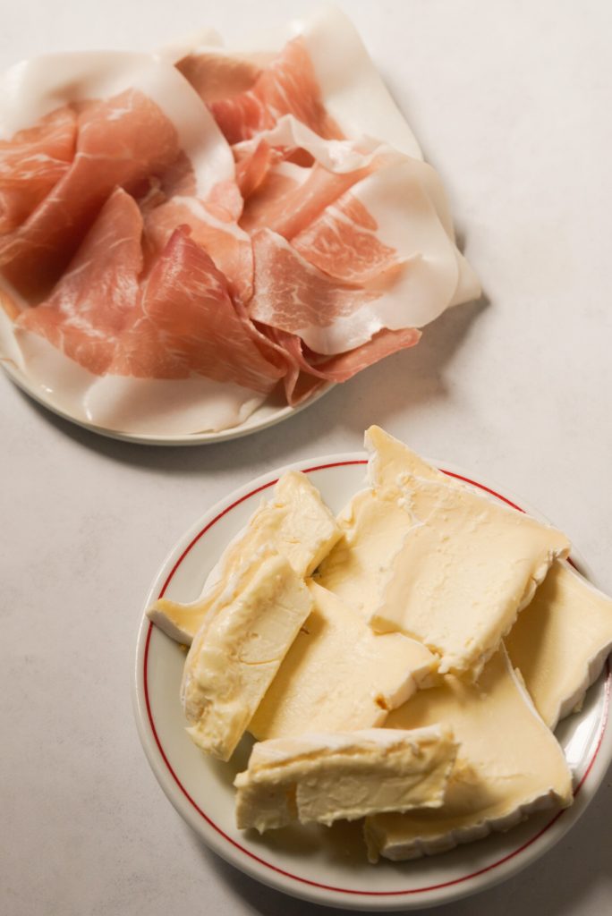 prosciutto and brie cheese on a white table