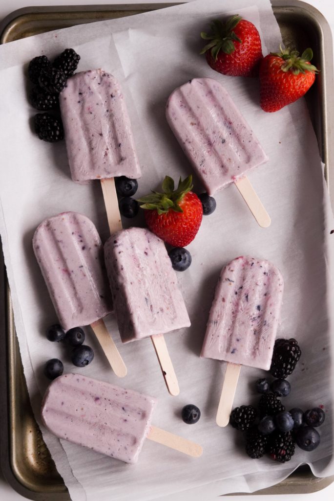 berry popsicles with protein on a parchment paper lined baking tray with fresh berries