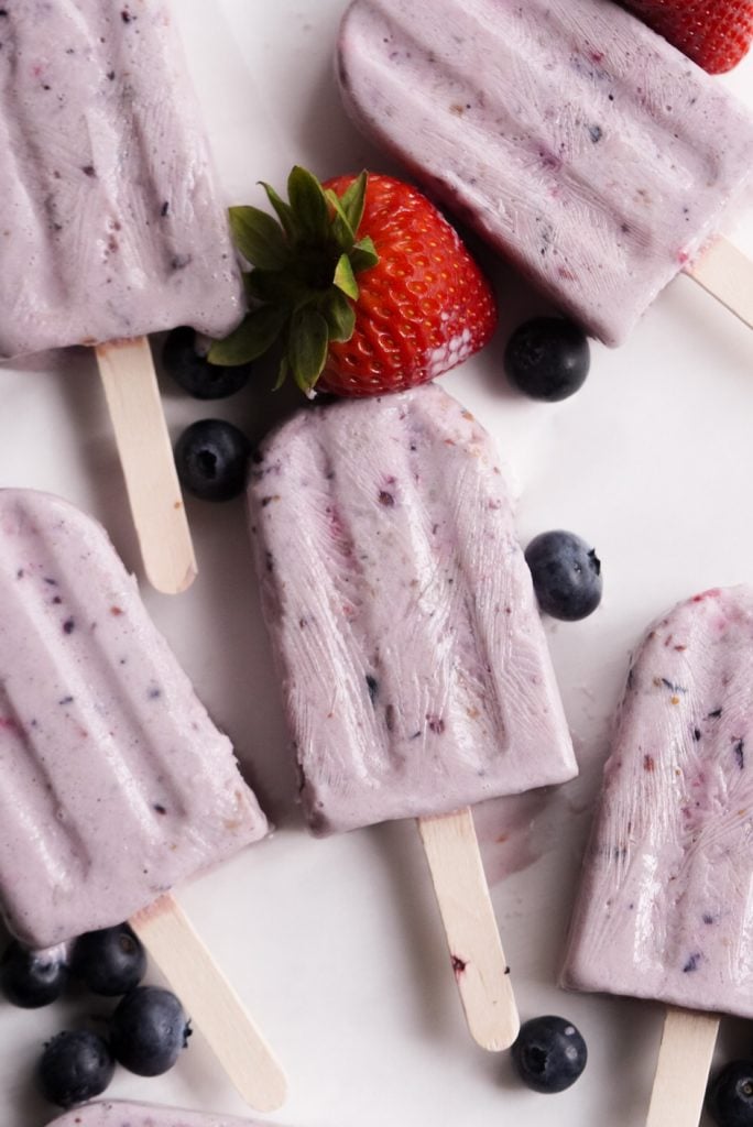 protein popsicles on a white surface with berries surrounding them