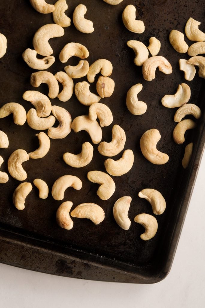 raw cashews spread out on a baking sheet.