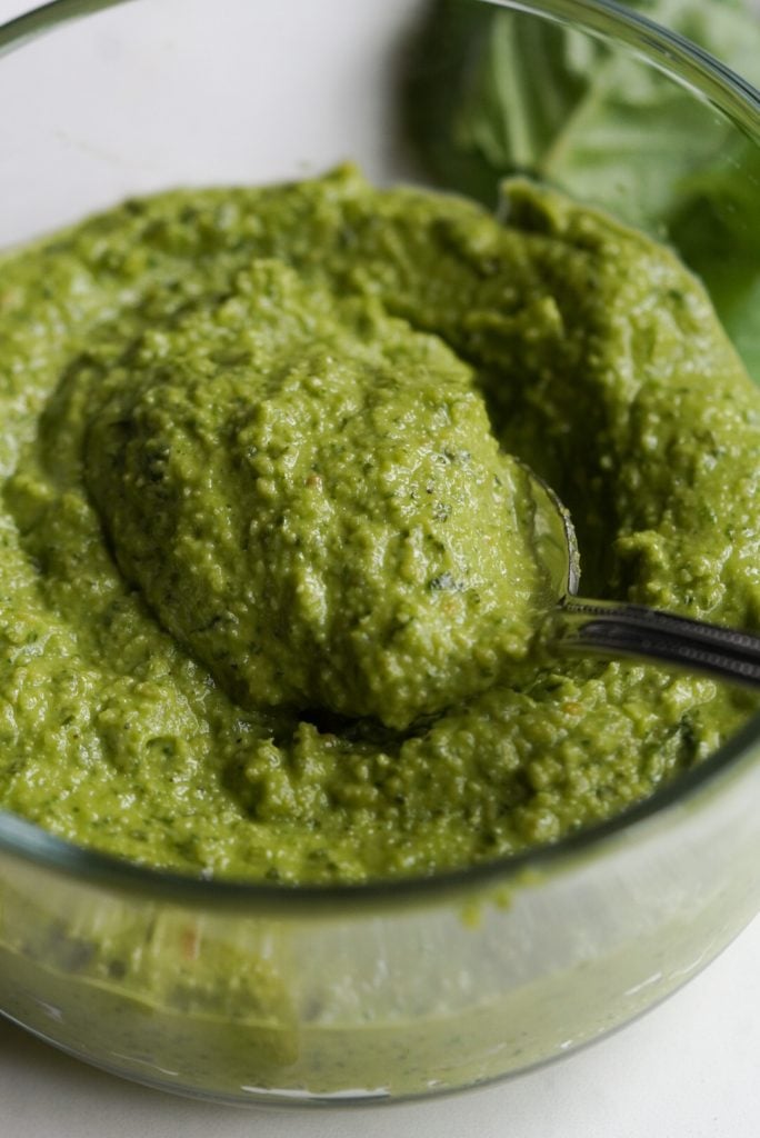 45 degree angle shot of a bowl of basil cashew pesto without pine nuts and a spoon taking a scoop out of it.