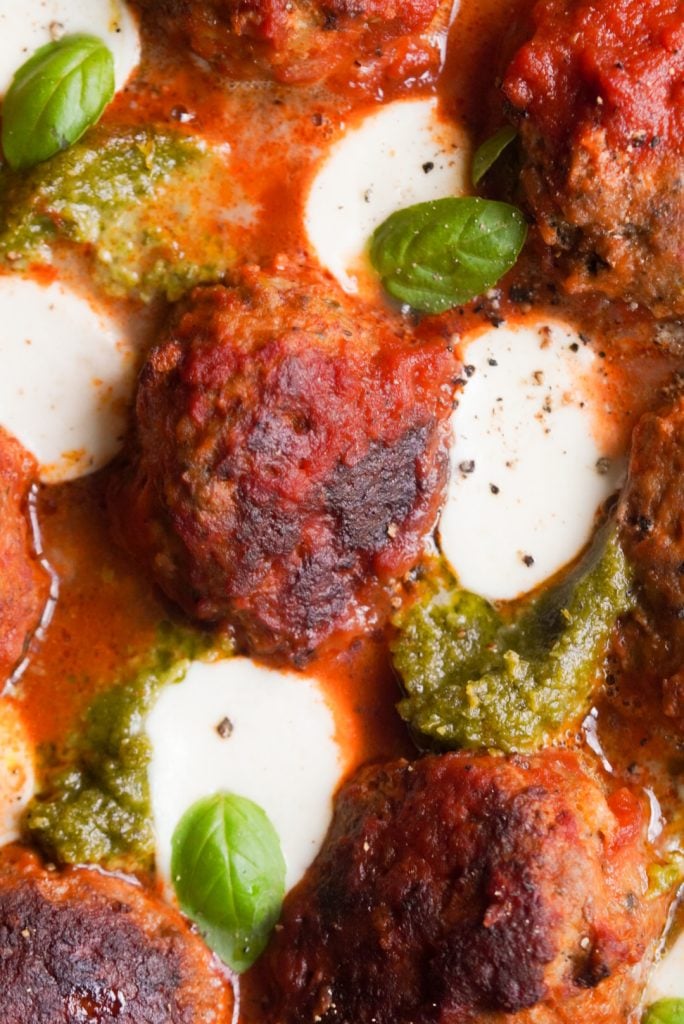 closeup overhead shot of a browned turkey pesto meatball in marinara sauce.