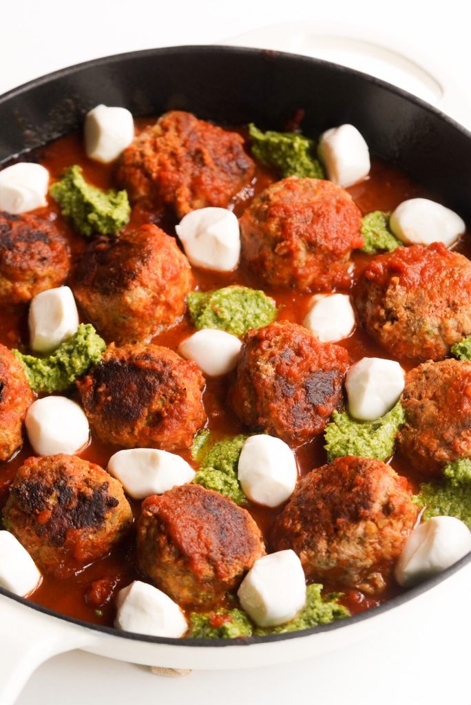mozzarella balls and pesto dollops have been added to the skillet for baking.