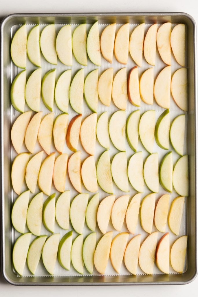 thin apple slices on a parchment paper lined baking sheet