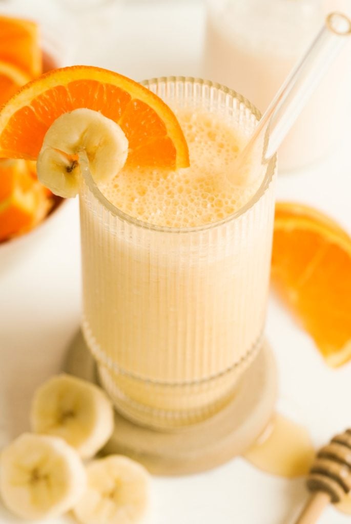 banana and orange banana smoothie in a glass with a glass straw