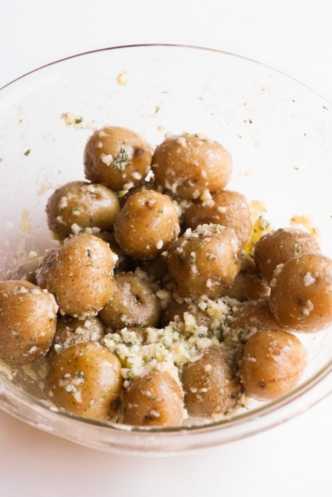 boiled baby potatoes mixed with garlic, olive oil, parmesan cheese, and parsley in a mixing bowl