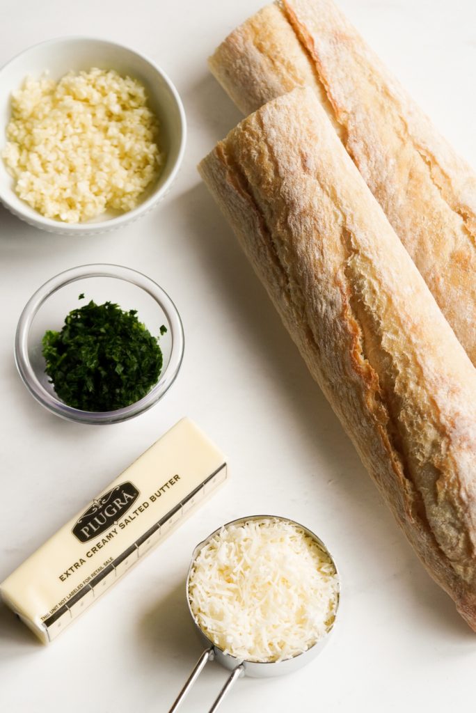 ingredients needed to make garlic bread baguette on a white table.