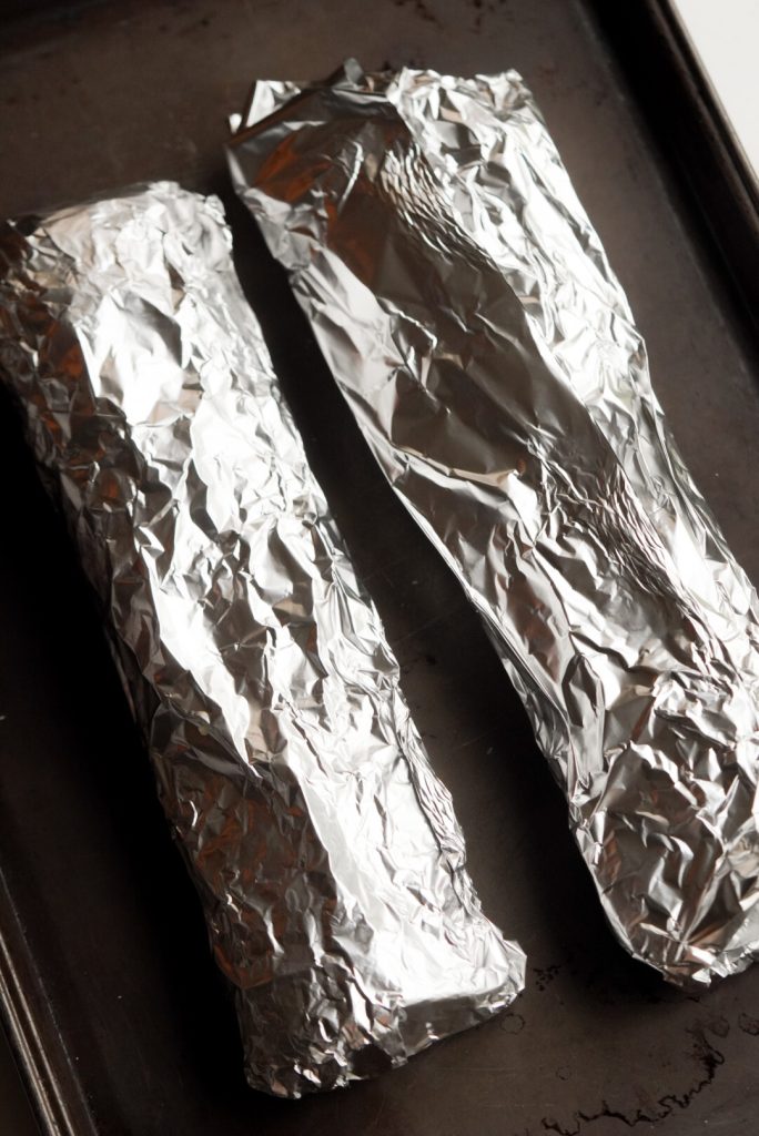 process shot — foil-wrapped baguette halves on a baking sheet.