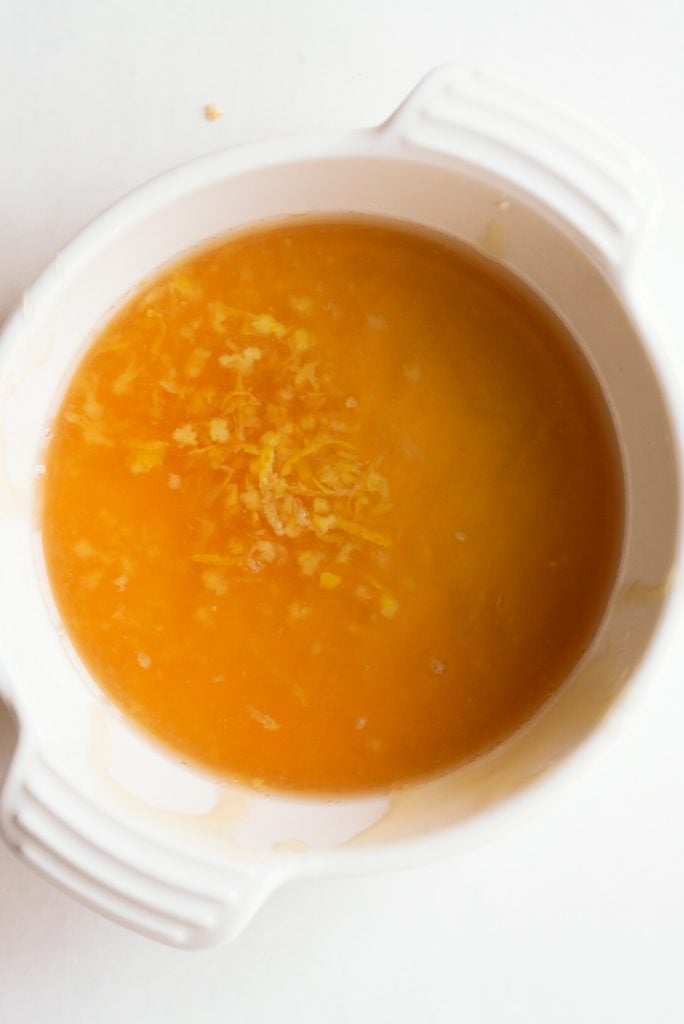 overhead shot of honey lemon fruit salad dressing ingredients added to a small white bowl.