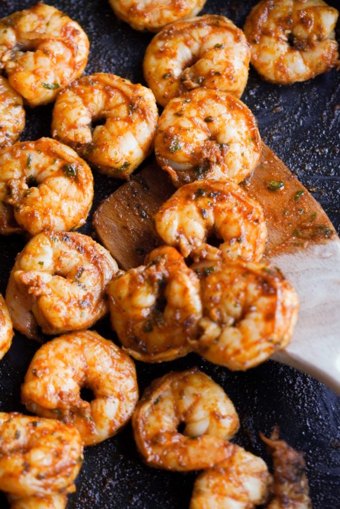 wooden spatula turning baja shrimp on a cast iron skillet.