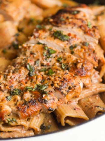 sliced seasoned chicken breast on top of a skillet filled with creamy sundried tomato pasta.