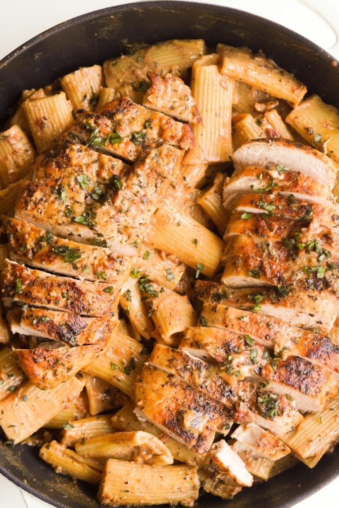 overhead shot of two sliced chicken breasts on a bed of creamy sun dried tomato pasta.