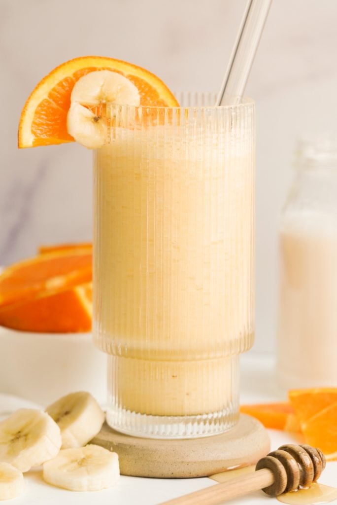 orange banana smoothie in a glass surrounded by banana and orange slices