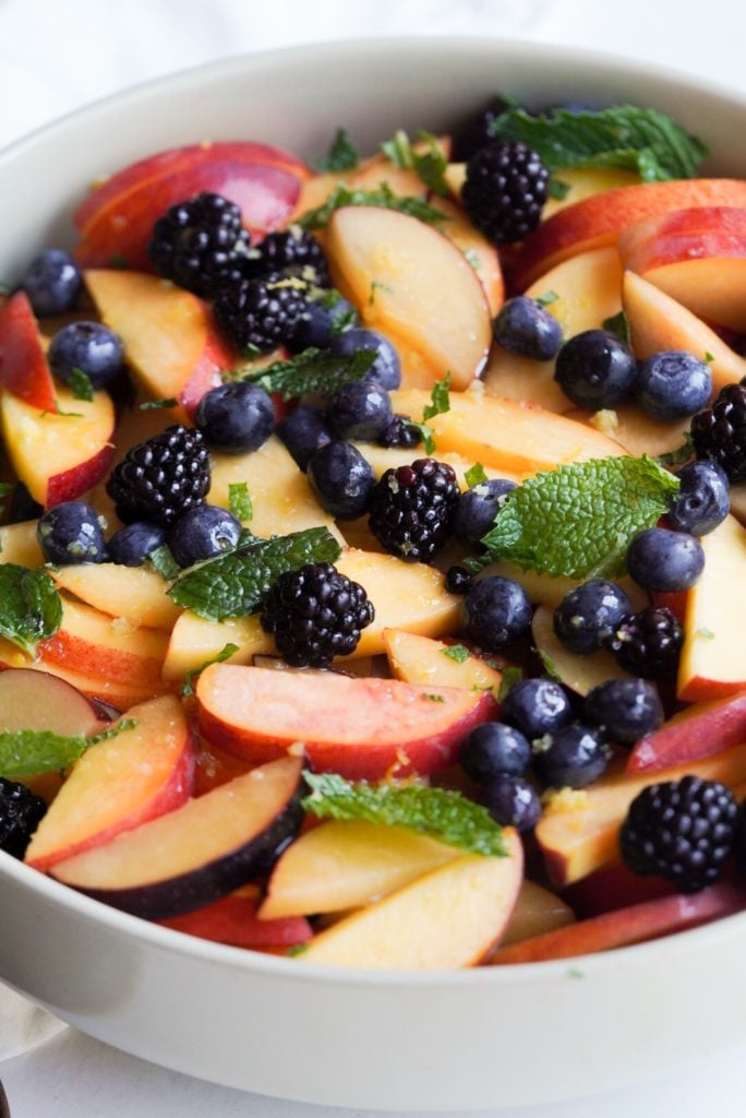 white serving bowl filled with stone fruit salad and garnished with fresh berries and mint.
