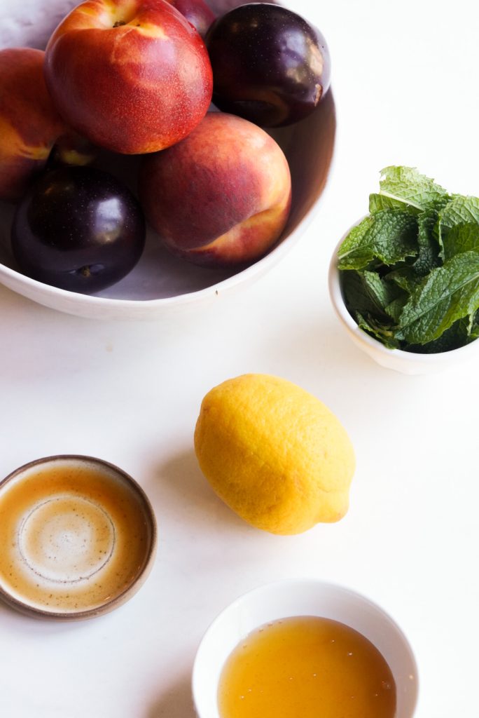 ingredients needed to make stone fruit salad and honey lemon dressing on a white table.