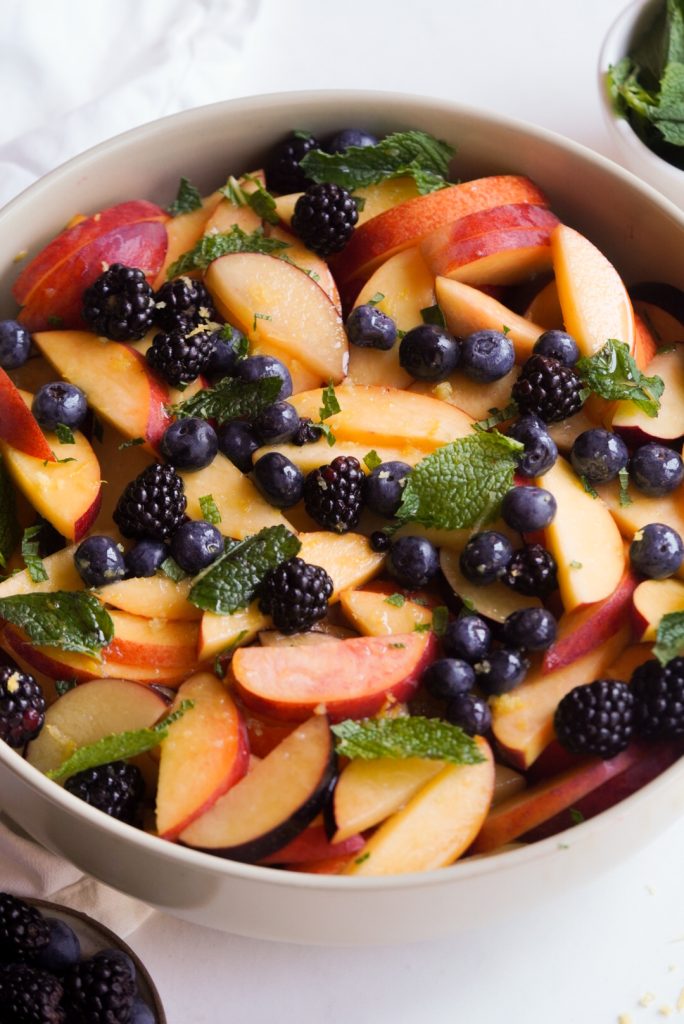 overhead shot of a serving bowl of stone fruit salad with berries, mint, and honey lemon dressing.