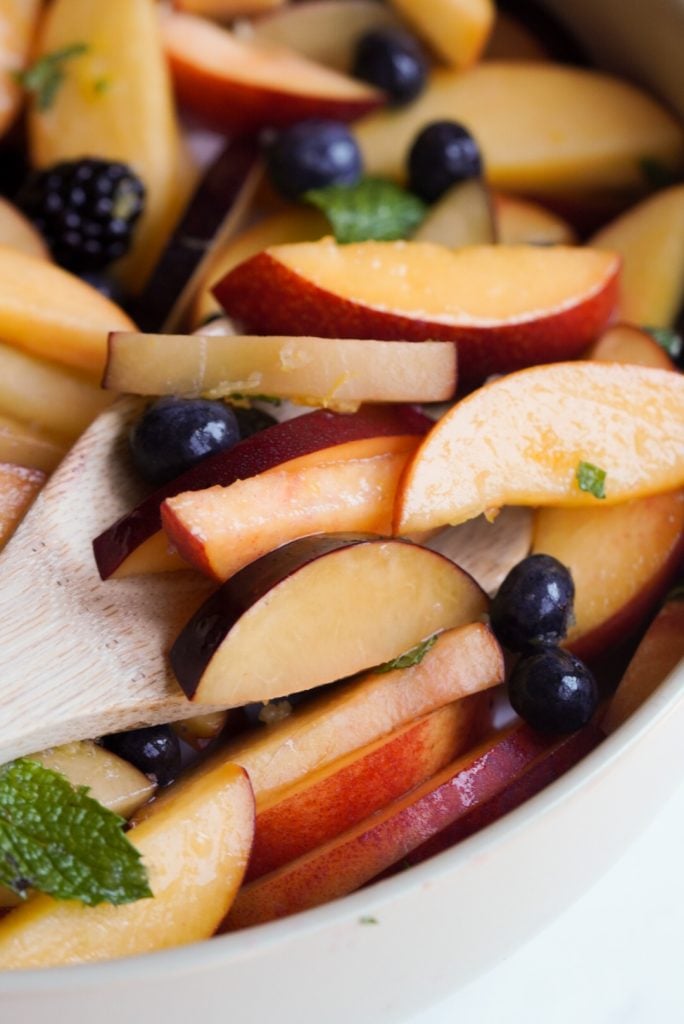 closeup shot of a wooden spoon taking a scoop of the stone fruit salad.