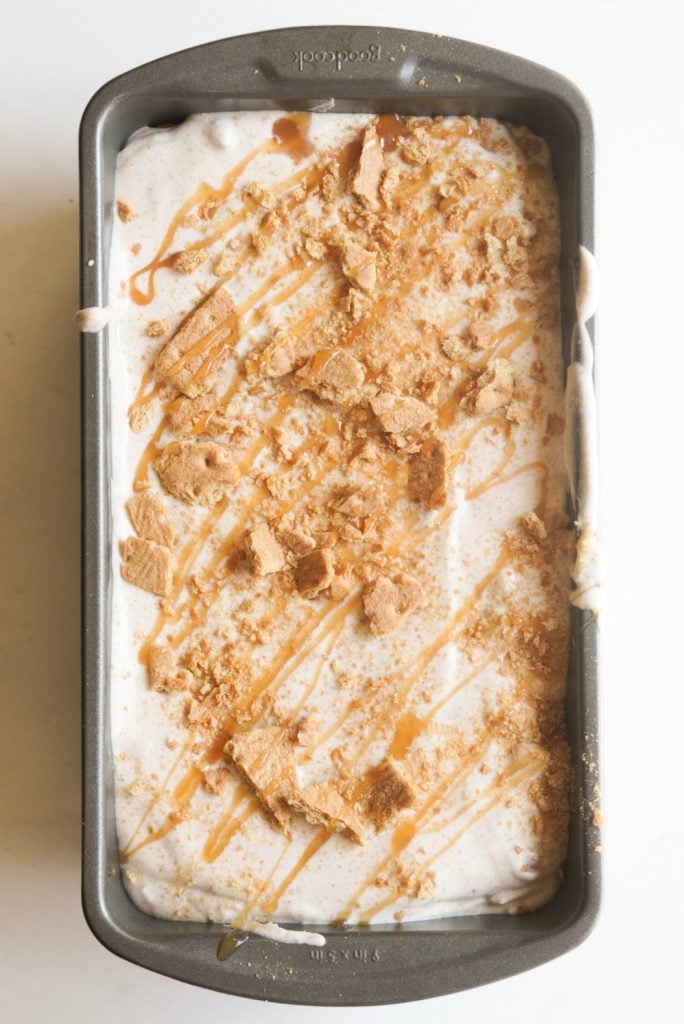 process shot - caramel apple pie ice cream packed into a loaf tin and topped with crushed graham crackers and a caramel drizzle before freezing.