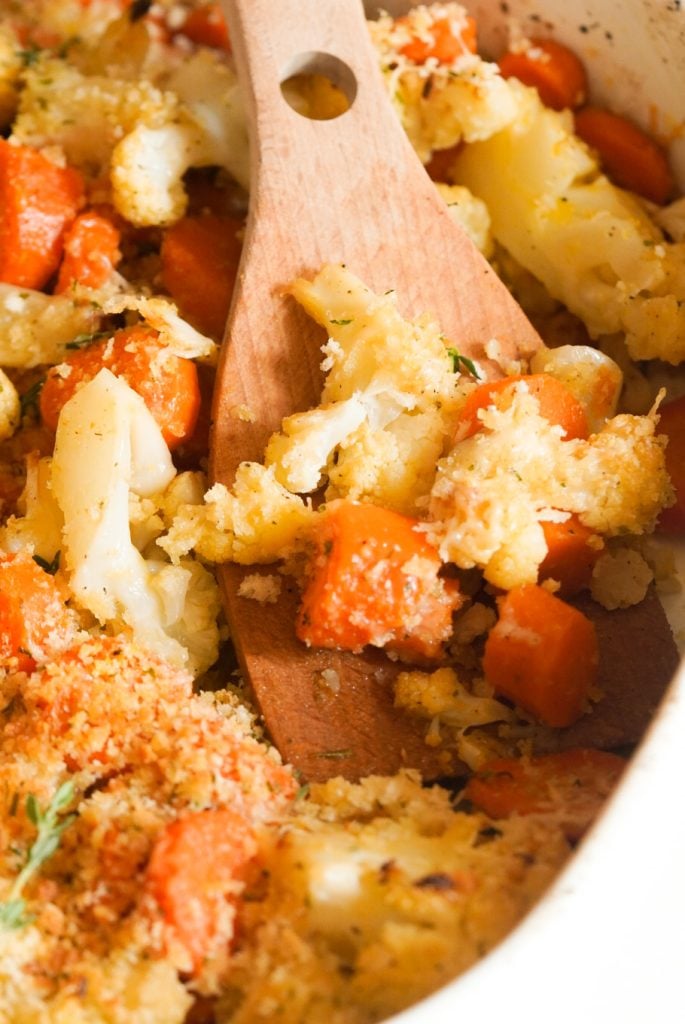 closeup shot of a wooden spoon taking a serving of roasted carrots and cauliflower.