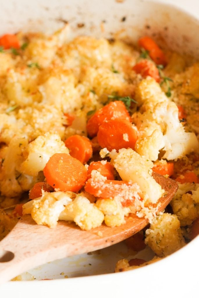 taking a serving of roasted carrots and cauliflower with a large wooden spoon.