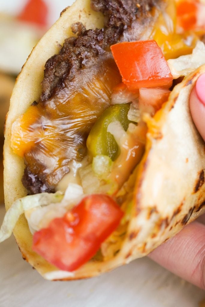 hand holding a smash taco with toppings and burger sauce