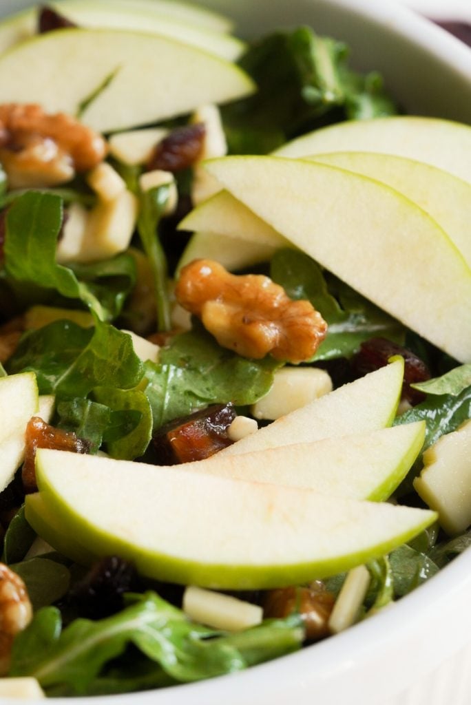 closeup vertical hero of an Apple Arugula Salad with Maple Balsamic Dressing and candied walnuts.