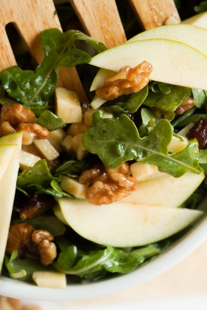 closeup overhead shot of a wooden salad fork grabbing a serving of apple arugula salad.