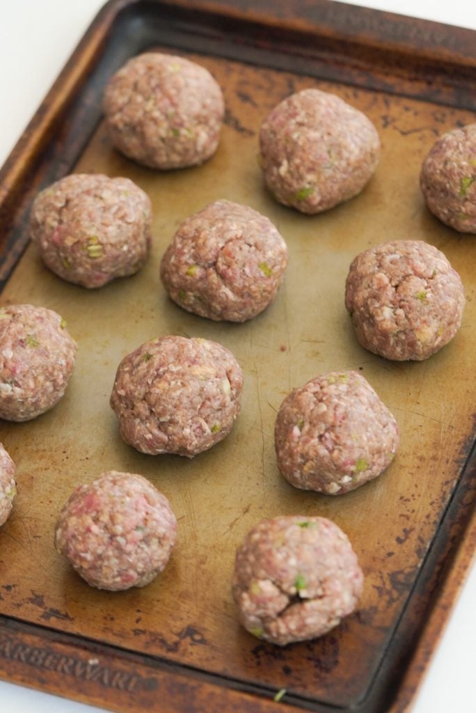 12 raw meatballs rolled and placed on a baking sheet.