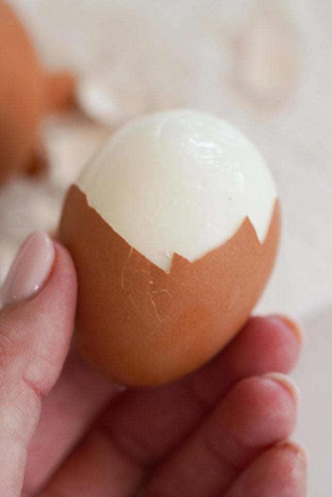 hand holding a halfway peeled soft boiled egg