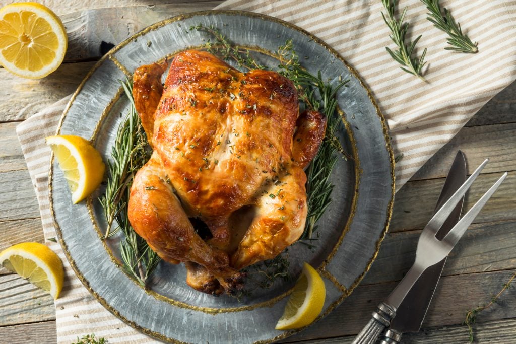 overhead shot of a rotisserie chicken on a plate on a wooden table