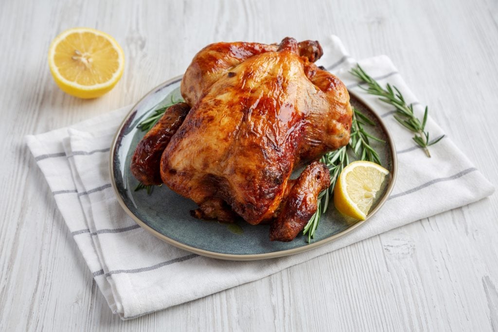 rotisserie chicken on a plate with lemon wedges and fresh herbs