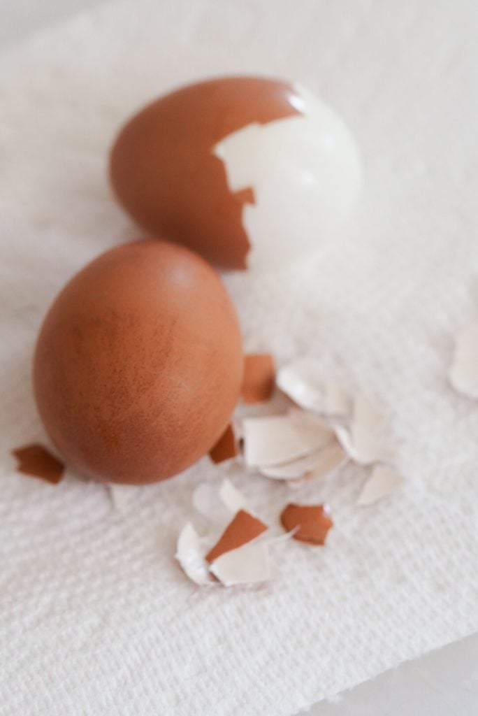 two boiled eggs on  a paper towel, one partially peeled